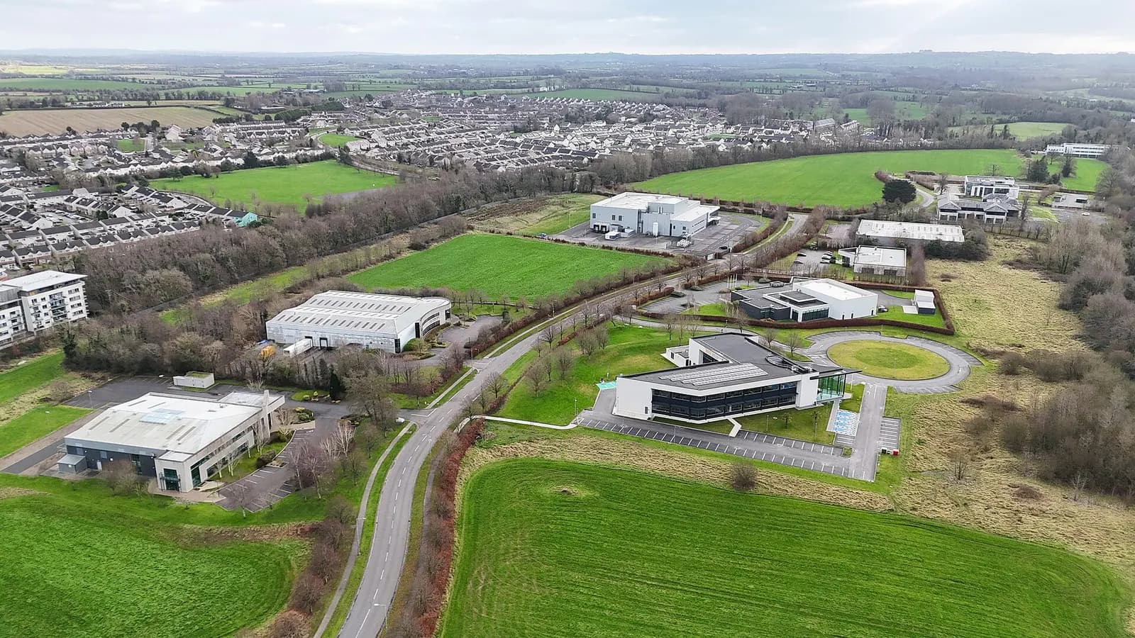 Vue aérienne d'un parc d'activités avec bâtiments d'entreprise et entrepôts entourés de champs verts